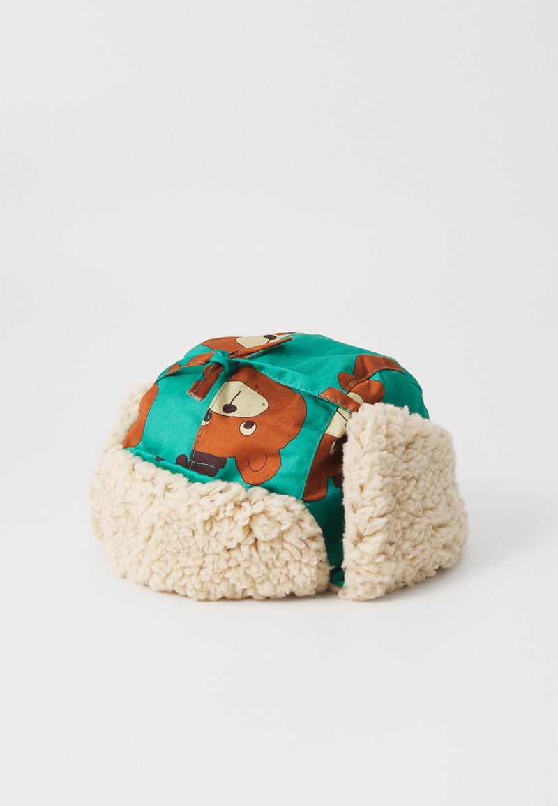 Chapeau en tissu vert avec imprimé de ours en cartoon, doublé de fausse fourrure couleur crème, de forme arrondie et avec un nœud ajustable sur le dessus.