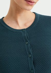 Teal knitted cardigan featuring a textured pattern, round neckline, and six matching buttons down the front.