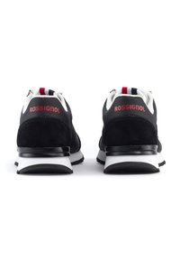 Zwarte sportieve schoenen van suede en mesh materialen, met een witte zool, een rood merklogo en een gestreepte stofaccent op de hiel.