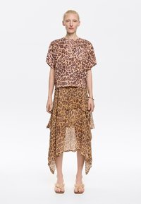 Leopard print crop top in light fabric, paired with a matching asymmetrical skirt. Sheer and layered design in earth tones. Flat sandals with floral accents.
