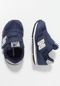 Tyrkysové sportovní boty z meshe a semiše s páskem na suchý zip, bílými akcenty a texturovanou gumovou podrážkou.