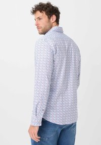 Lyseblå skjorte med lange ærmer og mønster af små røde og marineblå cirkler. Har en knap-ned krave og tætsiddende design.