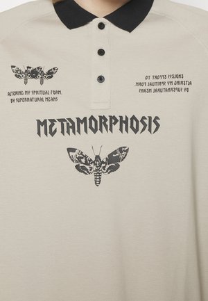 Polo beige avec col noir, illustrations de mites noires et texte stylisé : « MÉTAMORPHOSE » ainsi que des phrases sur la transformation de la forme spirituelle.