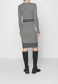 Grau gestreiftes Strickkleid mit langen Ärmeln, ausgestattet mit einem schwarzen horizontalen Streifen an der Taille und am unteren Saum. Schwarze kniehohe Stiefel.