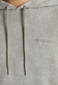 Felpa grigia chiara in tessuto morbido, con un motivo testurizzato, cordini regolabili e logo del marchio ricamato sul petto.