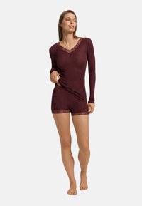 Bordowy top z długim rękawem z koronkowym wykończeniem przy dekolcie, w połączeniu z dopasowanymi szortami, z koronkowymi akcentami na dole. Miękki, dopasowany materiał.