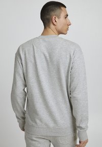 Sweatshirt gris en tissu doux et texturé. Doté d'un col rond, de poignets côtelés et d'un ourlet. Étiquette visible en bas à gauche.
