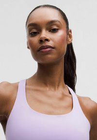 Ljuslila sportbh med rundad halsringning, breda remmar och en slät, elastisk textur som sitter tätt mot kroppen.