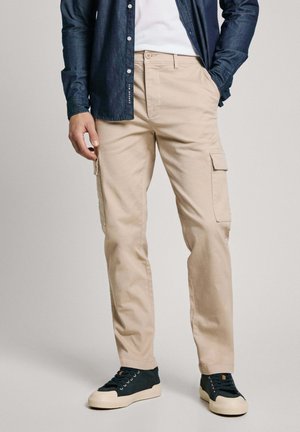 Beige cargobroek met zijzakken, gecombineerd met een marineblauw overhemd met knopen en donkergrijze sneakers met een crèmekleurige zool.