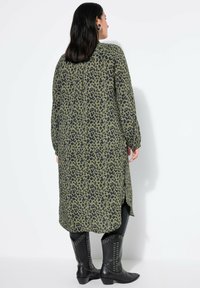 Vestido largo y holgado en verde oliva con estampado de leopardo negro. Presenta una gran abertura y mangas largas, confeccionado en una tela suave y texturizada.