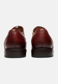 Braune Leder-Brogues mit detaillierten Perforationen, glatter Oberfläche und dunklem Holzabsatz. Die Rückansicht hebt die Nähte und das Design hervor.