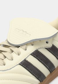 Crème-kleurige leren sneaker met donkergrijze suede strepen, een gestructureerde tong en gevlochten veters. Beschikt over een gumrubberen zool voor grip.