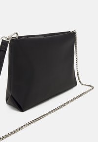 Černá syntetická psaníčko s hladkým povrchem, obdélníkovým tvarem a odnímatelným stříbrným řetízkovým popruhem. Má zipové otevírání na vrchu.