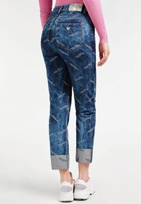 Jeansy denimowe w wyblakłym niebieskim kolorze z białymi literami, zwężanym krojem, podwiniętymi nogawkami i tylnymi kieszeniami. Dopasowane do białych tenisówek.