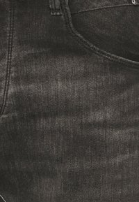 Jeans de mezclilla negra con una textura suave, un ligero desgaste y costuras estándar. Presentan un bolsillo frontal y un diseño clásico de cintura.