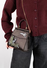 Sac à main en satin marron avec broderie d'un loup et d'éléments célestes. Il présente une forme structurée, une poignée supérieure et une longue bandoulière en chaîne dorée.