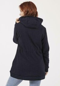 Sweat-shirt à capuche navy avec une taille élastique, tissu texturé et une bande décorative le long de l'ourlet. Détails de couture au dos.