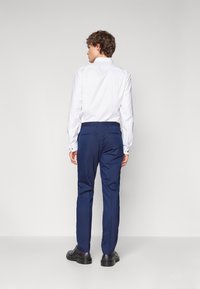 Navy trousers with a slim fit design, crafted from a smooth fabric. Features side pockets and a subtle texture. Worn with a white shirt.