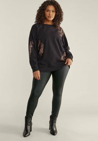 Zwarte sweatshirt met sequins op de mouwen, gecombineerd met glanzende zwarte leggings en enkellaarsjes. Zachte stofstructuur en een relaxte pasvorm.