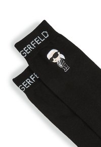 Calze nere con una figura dei cartoni animati che indossa occhiali da sole e un completo, con testo bianco "LAGERFELD" in cima. Realizzate in materiale morbido e flessibile.
