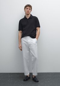 Černé polokošile, bílé kalhoty a černé mokasíny; ležérní střih s krátkým rukávem a dvoutlačítkovou légou; hladká tkanina a minimalistický design.