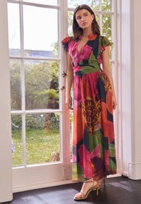 Maxikleid mit Blumenmuster, tiefem V-Ausschnitt, bunten Rosen- und Blättermustern, weichem Stoff und tailliertem Schnitt. Kombiniert mit beigen Riemchen-Highheels.