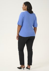 Pull bleu clair à manches courtes avec un ourlet côtelé, en tissu texturé, porté sur un pantalon noir ajusté et des chaussures à talons noires.