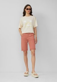 T-shirt jaune clair avec un graphisme de palmier ; shorts corail ; sandales compensées beige clair ; coupe décontractée ; ourlet roulé sur les shorts.