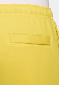Pantalones de chándal amarillos con una cinturilla elástica, que cuentan con un bolsillo trasero plano y una tela suave y texturizada.