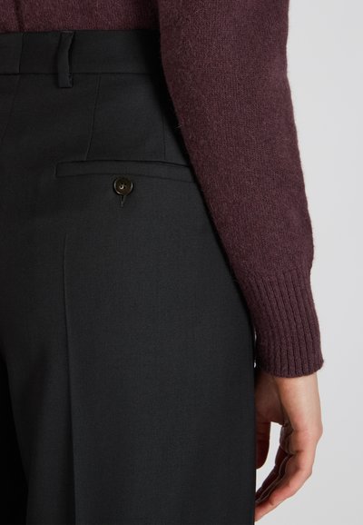 Czarne dopasowane spodnie o gładkiej fakturze, z tylną kieszenią z ciemnym guzikiem, w zestawieniu z rękawem bordowego swetra dzianinowego.