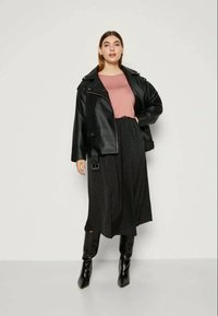 Casaco de cabedal preto de motociclista, camisa rosa, saia plissada preta e botins pretos brilhantes. Design moderno com texturas e contrastes distintos.