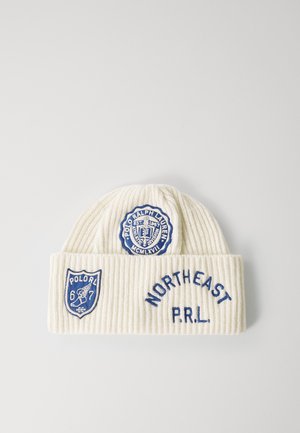 Caciula albă din tricot cu model rib, având logo-uri și text brodate în albastru. Accentele includ un logo circular și un design în formă de scut cu numere.