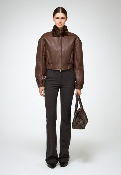 Bruine leren bomberjack met een bontkraag, gecombineerd met donkergrijze flare-broeken en een gestructureerde grijze handtas.