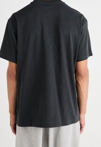 Schwarzes Baumwoll-T-Shirt mit Rundhalsausschnitt, kurzen Ärmeln und lässiger Passform, von hinten gezeigt, mit glatter Textur und ohne sichtbare Markenkennzeichnung.