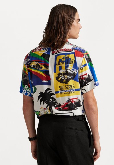 Camisa de manga corta con un diseño gráfico colorido de carreras, que incluye varias ilustraciones de coches, palmeras y texto sobre un fondo claro.