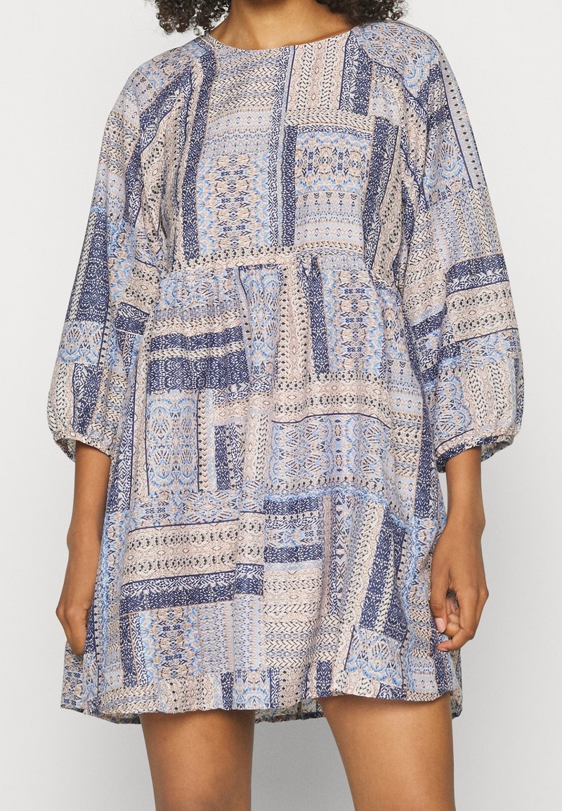 Leichtes, gemustertes Kleid aus einer Mischung von blauen und beigen Stoffen, mit rundem Ausschnitt und 3/4-langen Puffärmeln. Mit Taschen.