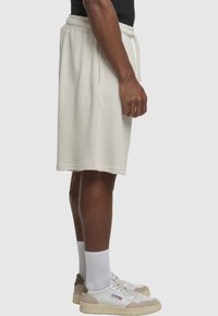 Lysebeige shorts med elastisk taljebånd og snøre. Vaffelstruktur, længde over knæet. Kombineret med hvide sokker og sneakers.