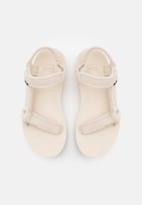 Beige sandals featuring a soft textured strap design and adjustable closures. The soles are flat and smooth, made for comfort and ease of wear.