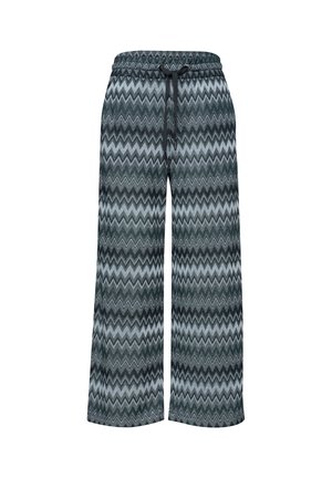 Close-up van donkergroene en grijze zigzagpatroon broek met een taillekoord en zakken, gedragen met een bleke top.