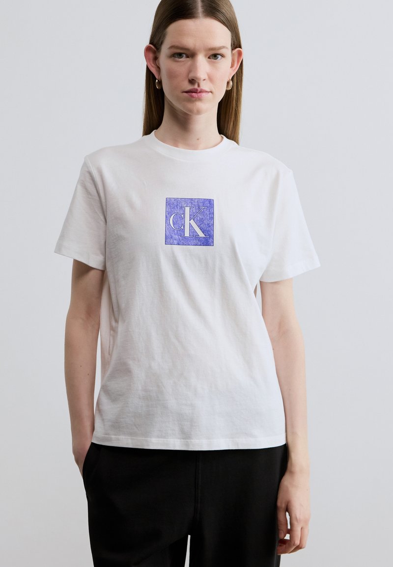 Λευκό βαμβακερό T-shirt με μοβ τετράγωνο λογότυπο στο κέντρο με το κείμενο "cK". Κλασικός στρογγυλός λαιμός και κοντά μανίκια, άνετη εφαρμογή.