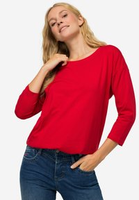 Rode lange mouwen T-shirt met een brede halslijn en een relaxed fit, gecombineerd met blauwe spijkerbroeken, wat een casual uitstraling geeft.