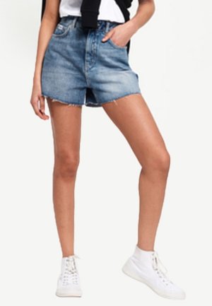 Person iført lyseblå denimshorts, hvide høje sneakers og en sort sweater bundet om taljen.