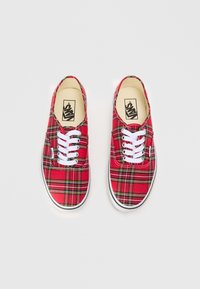Červené kockované tenisky s bielymi šnúrkami, s nízkym dizajnom a gumovou podrážkou. Vzor obsahuje čierne a žlté akcenty.