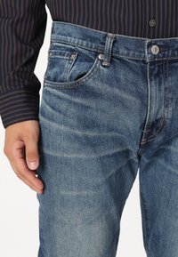 Jeans de mezclilla de color azul claro con corte recto, que presentan un diseño clásico de cinco bolsillos, sutiles desgastes y detalles de costura en contraste.