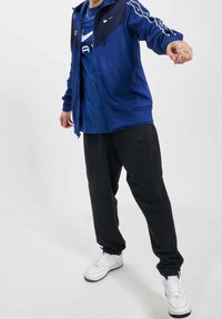 Blå zip-jacka med mörka ärmar, svarta sweatpants och vita sneakers. Har Nike-logotyper och en bekväm passform.