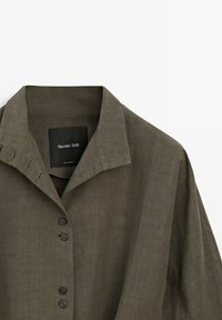 Olivgrön linneskjorta med krage, knappstängning framtill och dekorativ sömnad på axeln. Märke: Massimo Dutti.