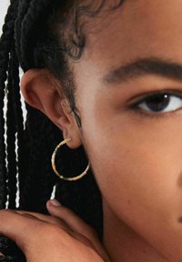 Beaded hoop earring made of mixed color beads, featuring a circular shape with a slightly textured surface, worn on a model's ear.