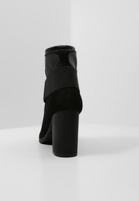 Stivale alla caviglia nero in suede e pelle con una fascia elastica. Presenta un tacco a blocco e una punta rotonda per un design elegante.