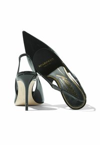 Zapatos de tacón alto de charol negro con puntera afilada, parte trasera abierta y una delgada correa en el tobillo. Logo dorado en la planta, detalles texturizados a lo largo del borde.
