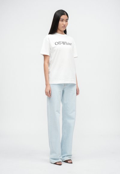 Valge puuvillane T-särk, millel on musta värviga "Off-White" kiri, kombineeritud helesiniste, sirge lõikega teksadega. Mudel seisab ühetaolise tausta ees.